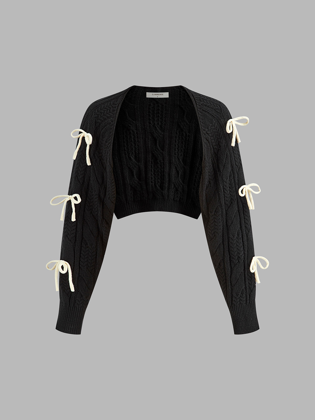 A black cropped cable knit cardigan with open front and three white ribbon bows per sleeve.