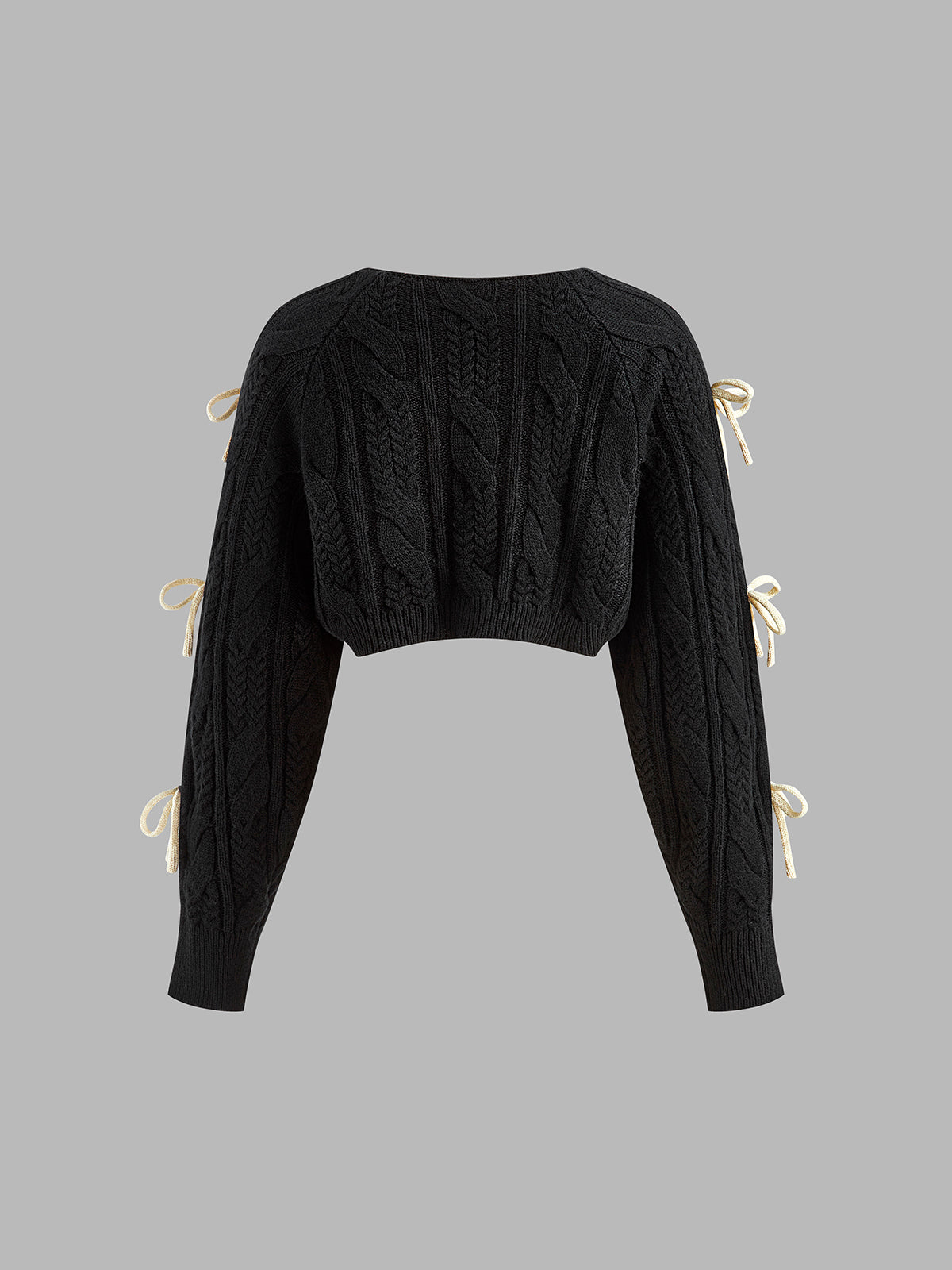 Black cropped cable knit cardigan with long sleeves and cream bow-knots accenting the sides.
