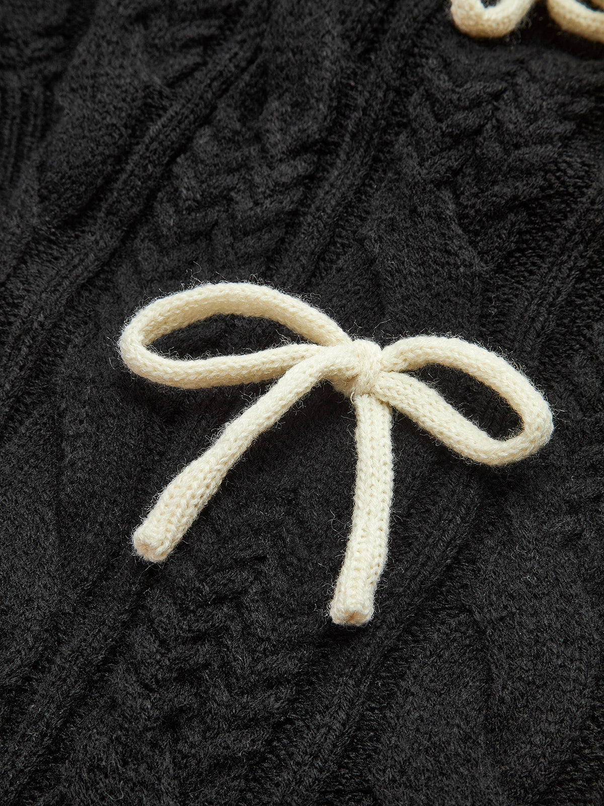 A black cable knit cardigan with intricate patterns and a white bow-knot accent on top.