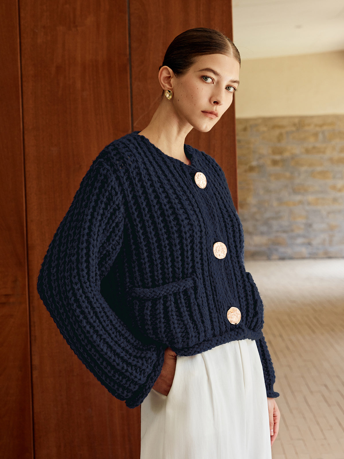 A relaxed navy soft knit cardigan with large gold buttons, styled over a white skirt.