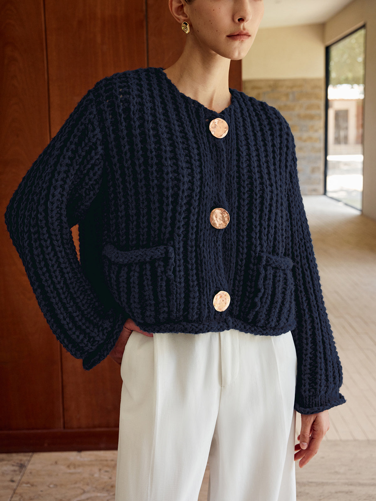 Chunky navy blue knit cardigan with large gold buttons, styled with white high-waisted trousers.