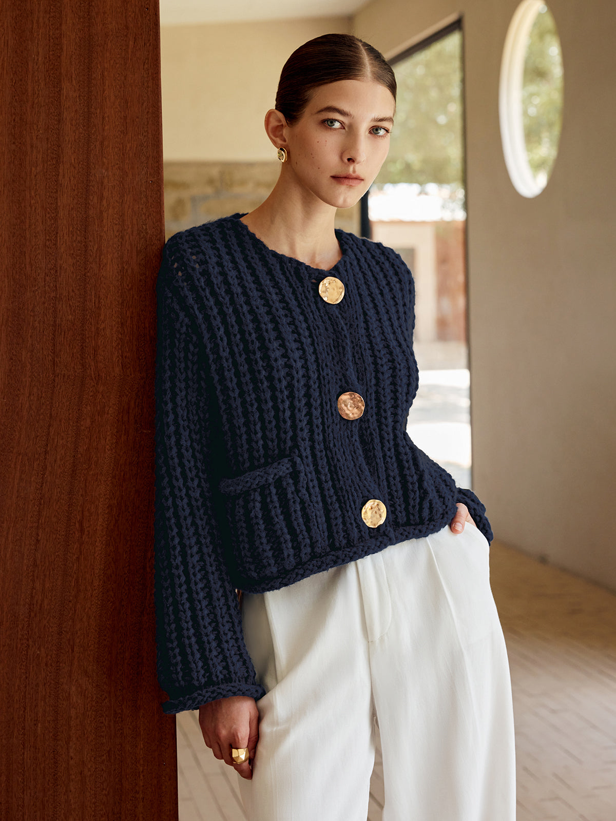 A soft knit button-up cardigan with large gold buttons, paired with white pants.