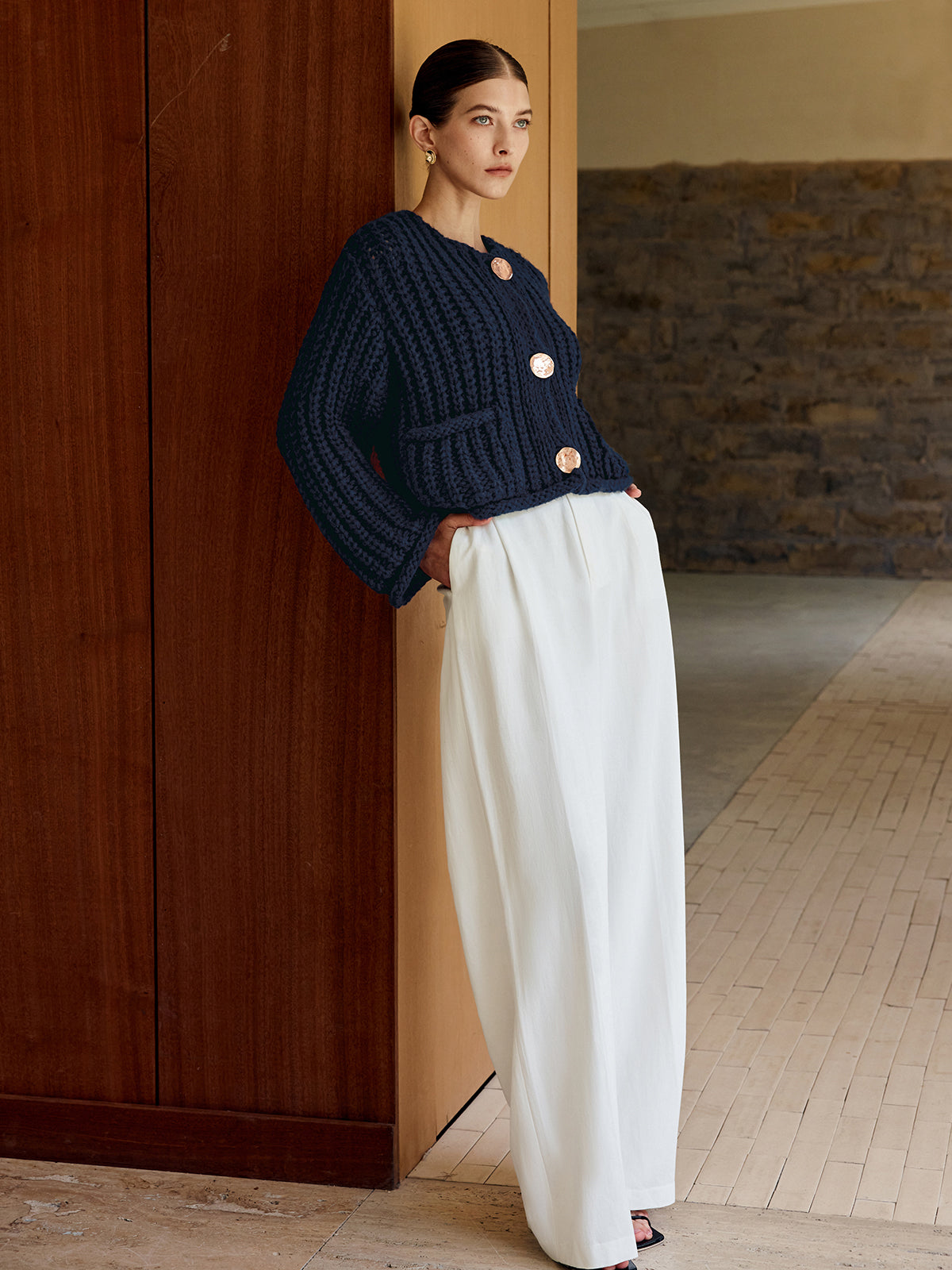 A soft knit button-up cardigan paired with wide-legged, high-waisted white trousers.