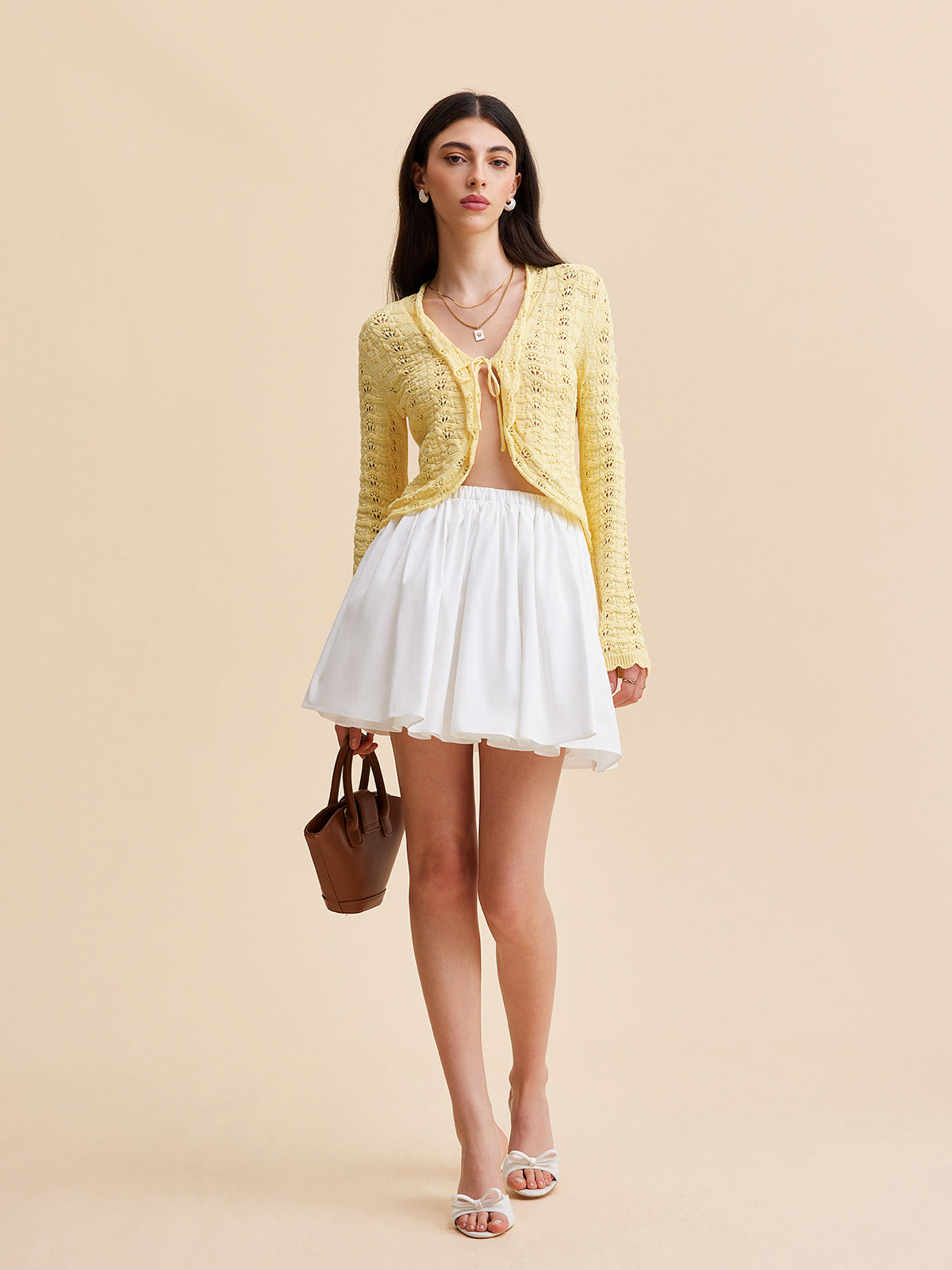 KOAD'CLO crocheted cardigan sweater with tie-front design, white mini skirt, and sandals.