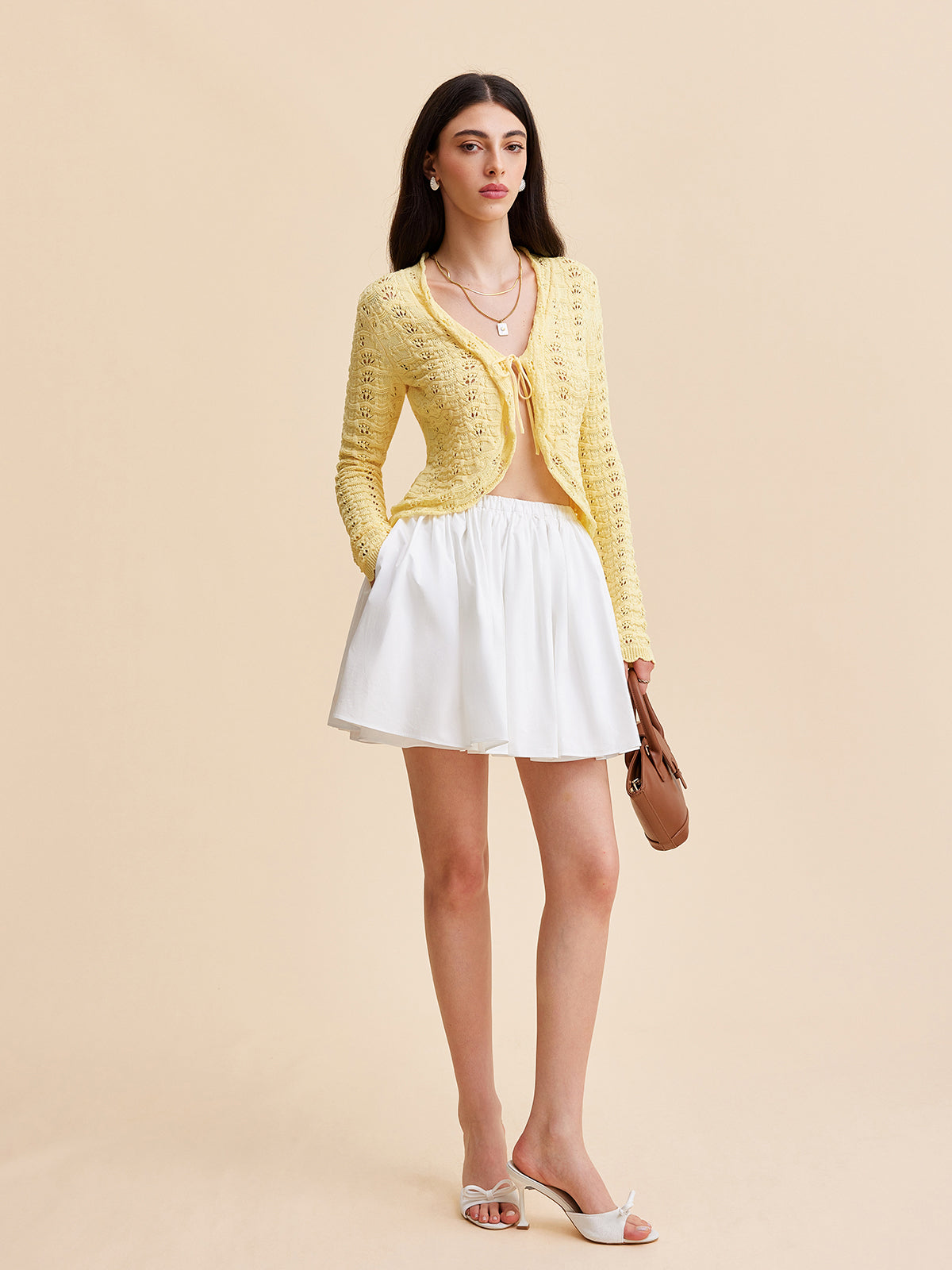 A crocheted cardigan sweater with a tie-front design, paired with a white skirt and sandals.