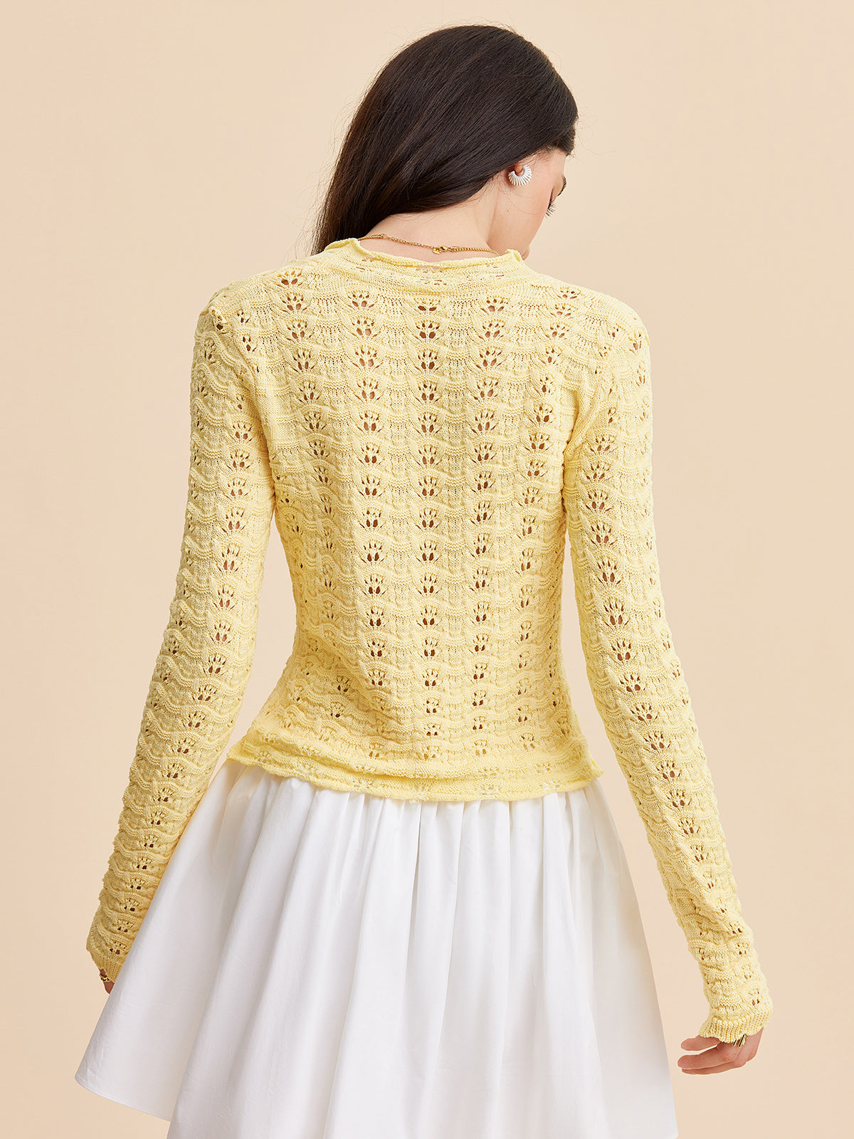 A pale yellow crocheted cardigan sweater with a tie-front design paired with a white skirt.