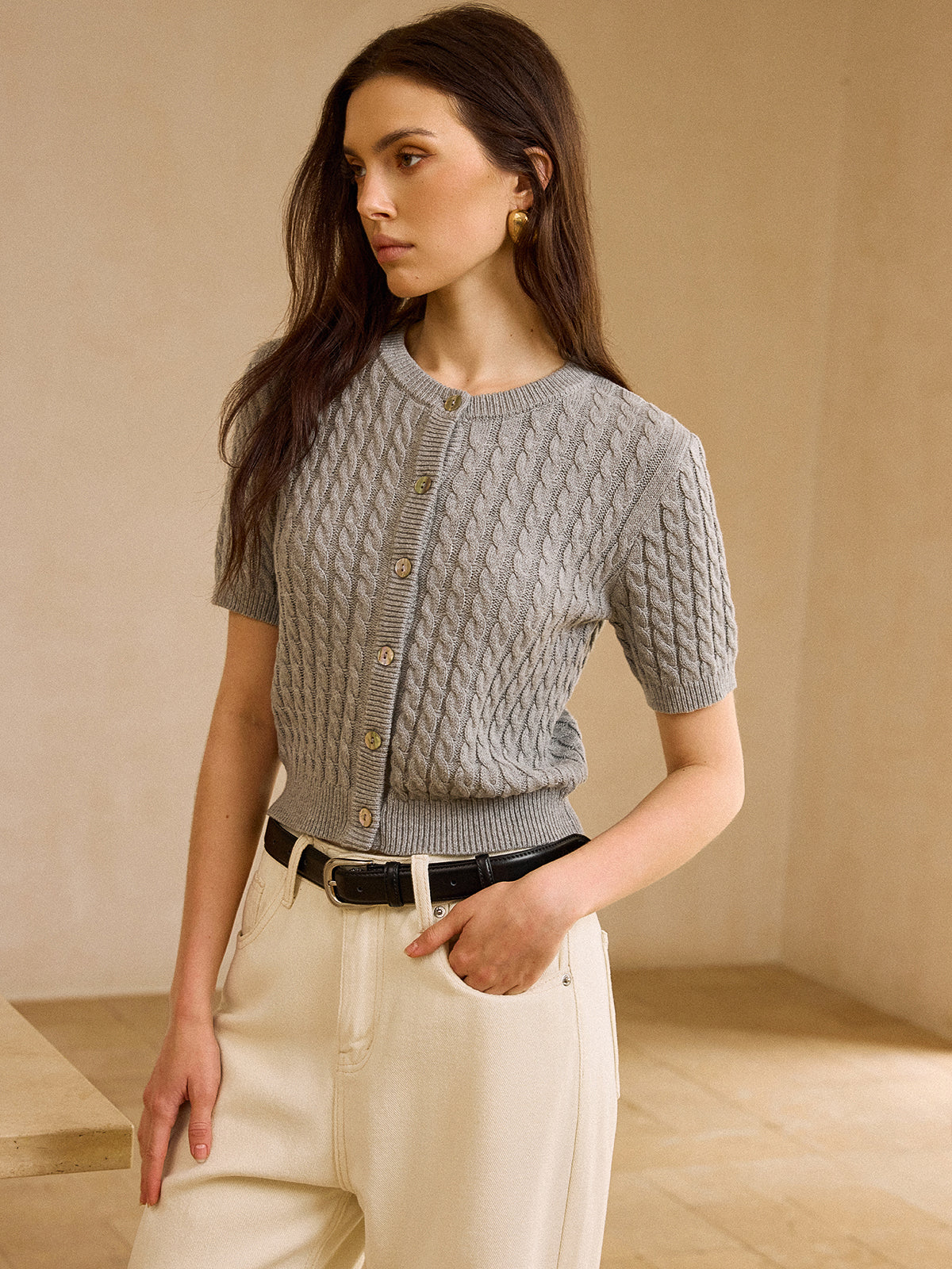 Short-sleeve cable knit cardigan sweater paired with cream high-waisted pants and black belt.