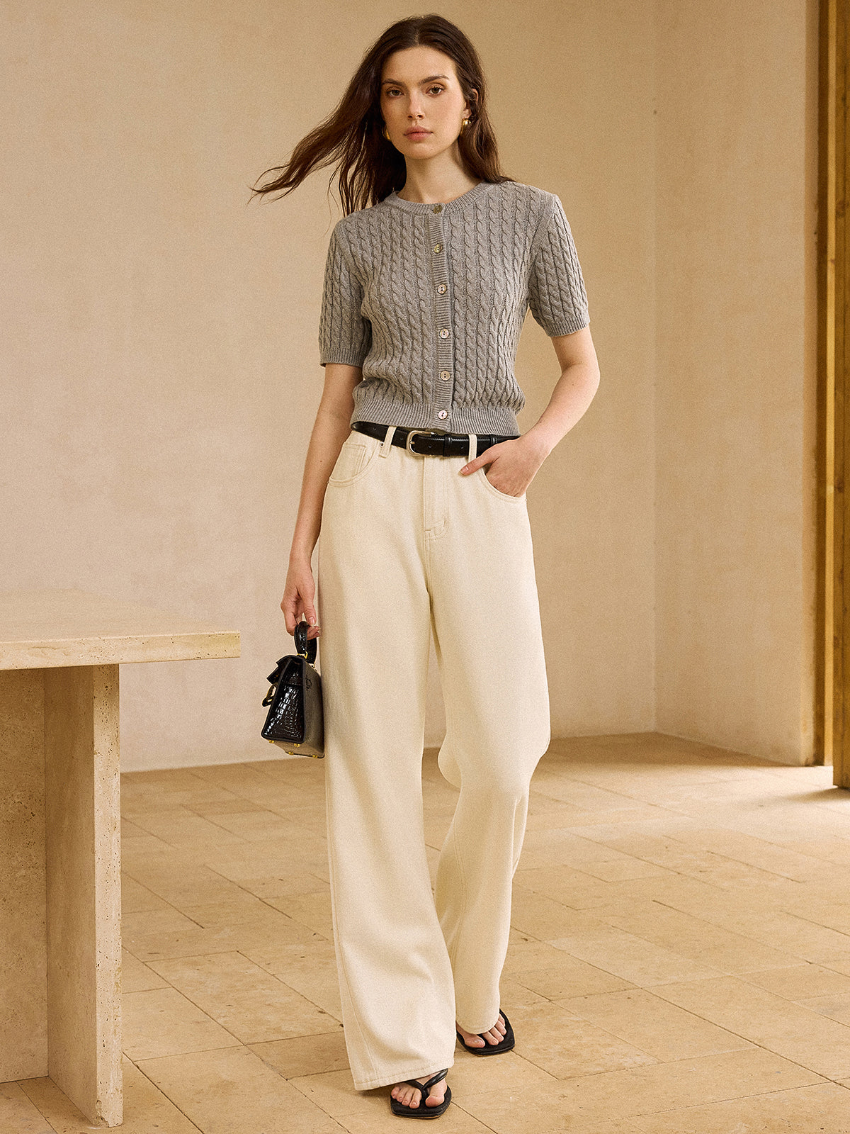 Short-sleeve cable knit cardigan sweater with cream wide-leg pants and a black belt.