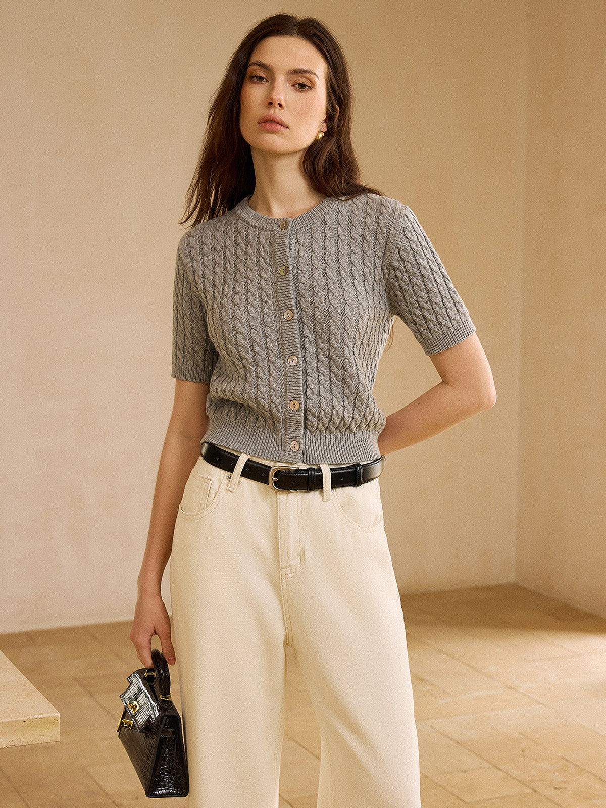 A cable knit short-sleeve cardigan sweater paired with high-waisted off-white jeans and black belt.