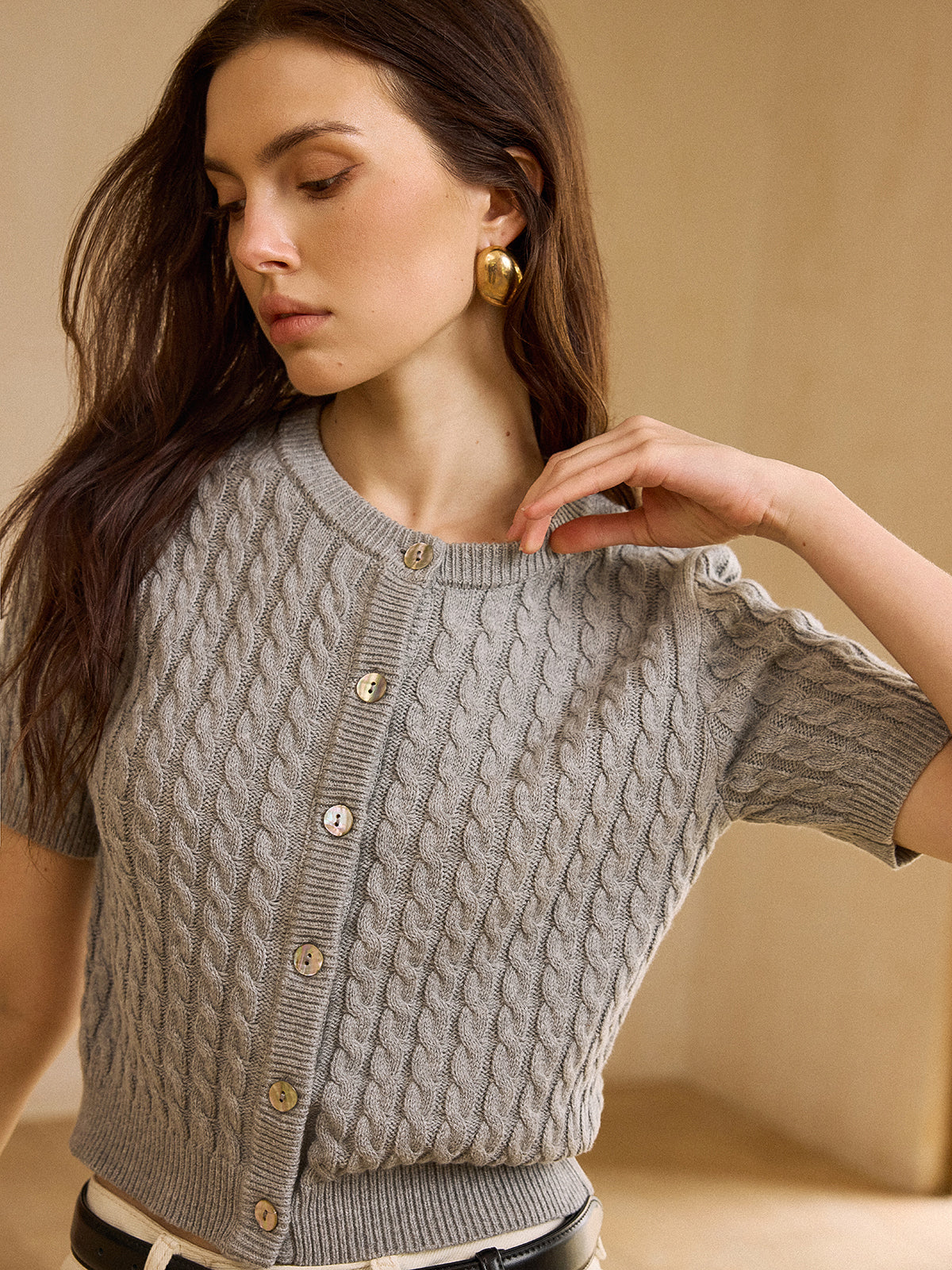 A short-sleeve cable knit cardigan sweater in a neutral tone with textured detailing.