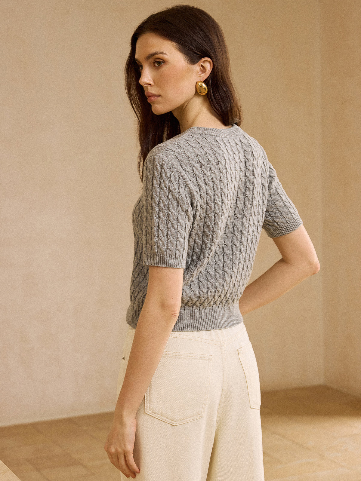 A cable knit short-sleeve cardigan sweater paired with cream high-waisted pants.