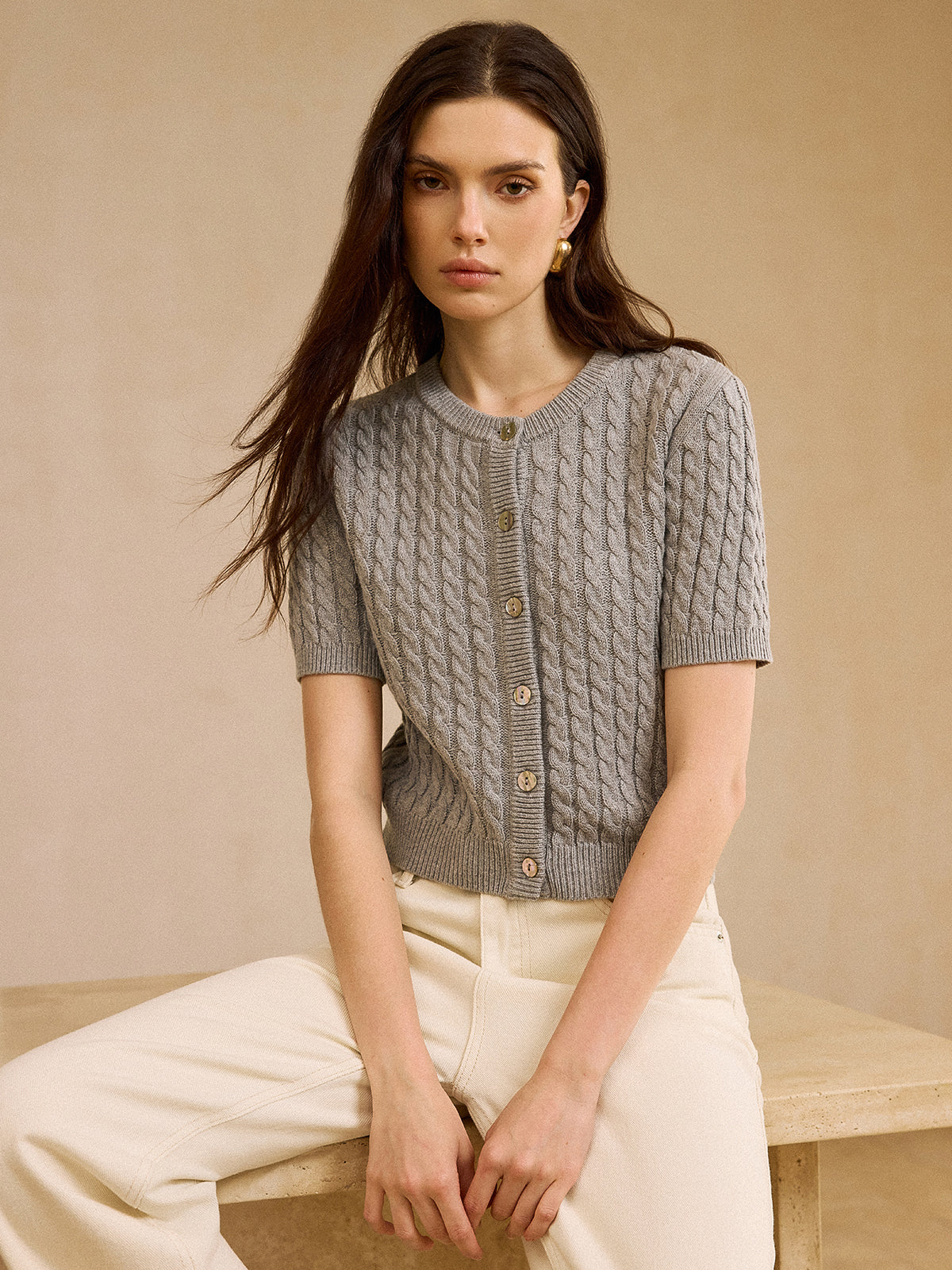 KOAD'CLO short-sleeve cable knit cardigan sweater paired with off-white pants.