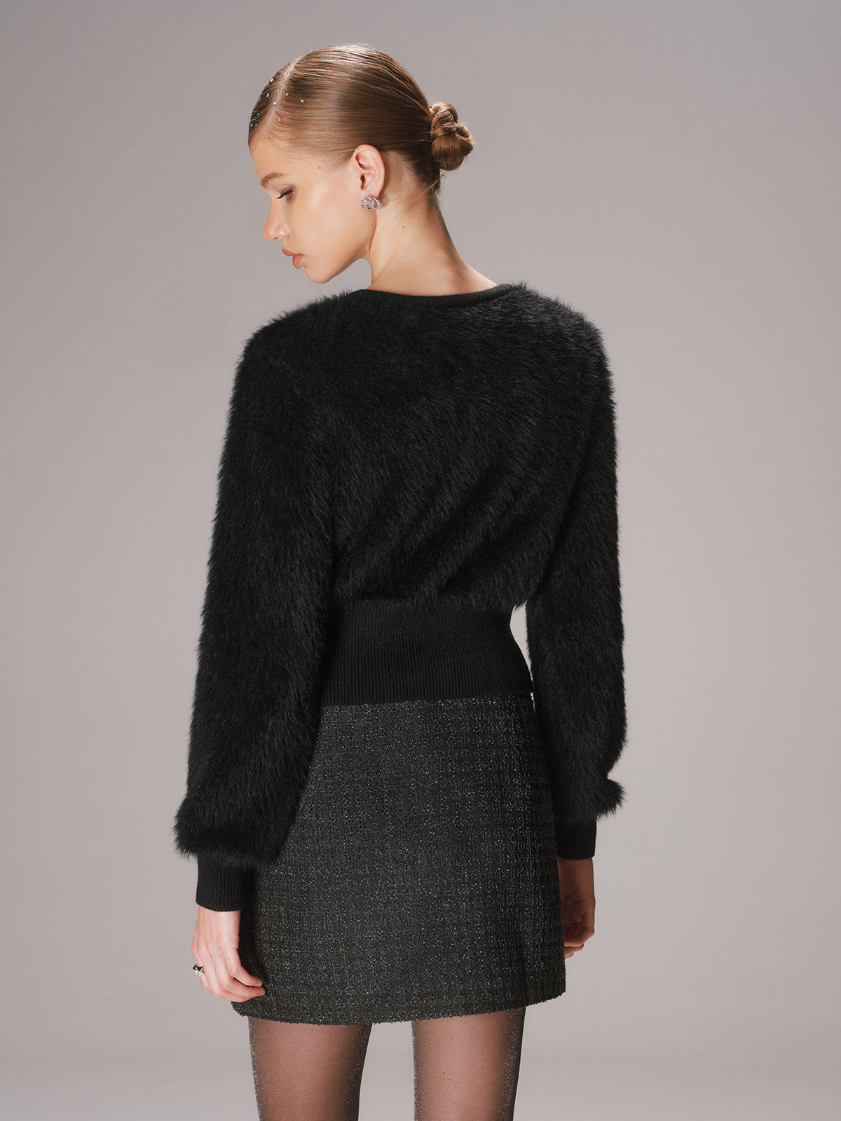 Cropped faux mink cardigan with button-front, worn over a dark textured skirt and sheer tights.